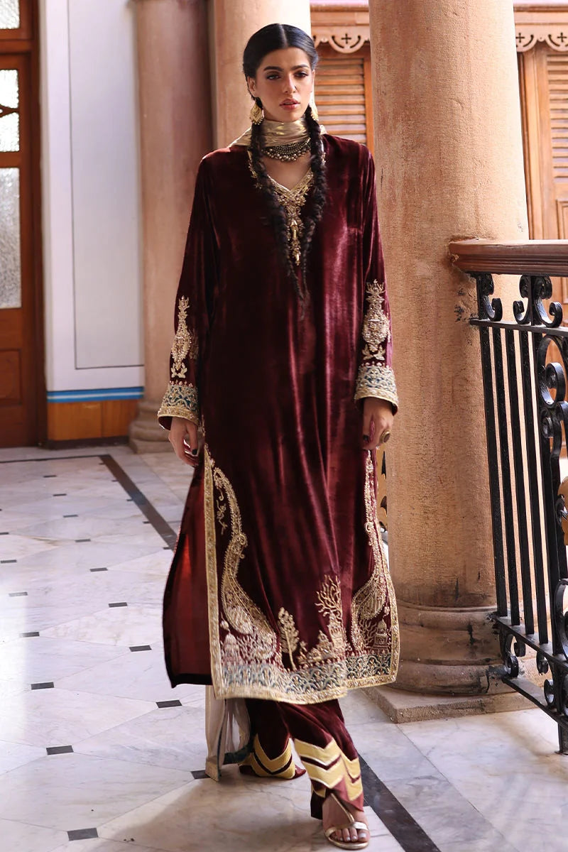 Woman in a traditional maroon and gold outfit standing in an elegant interior setting.