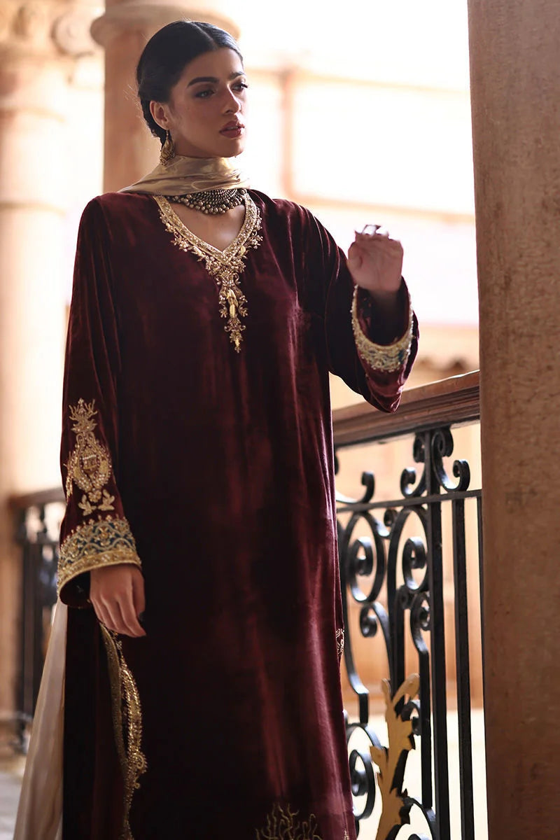 Woman in a burgundy traditional outfit with gold embroidery standing on a balcony.