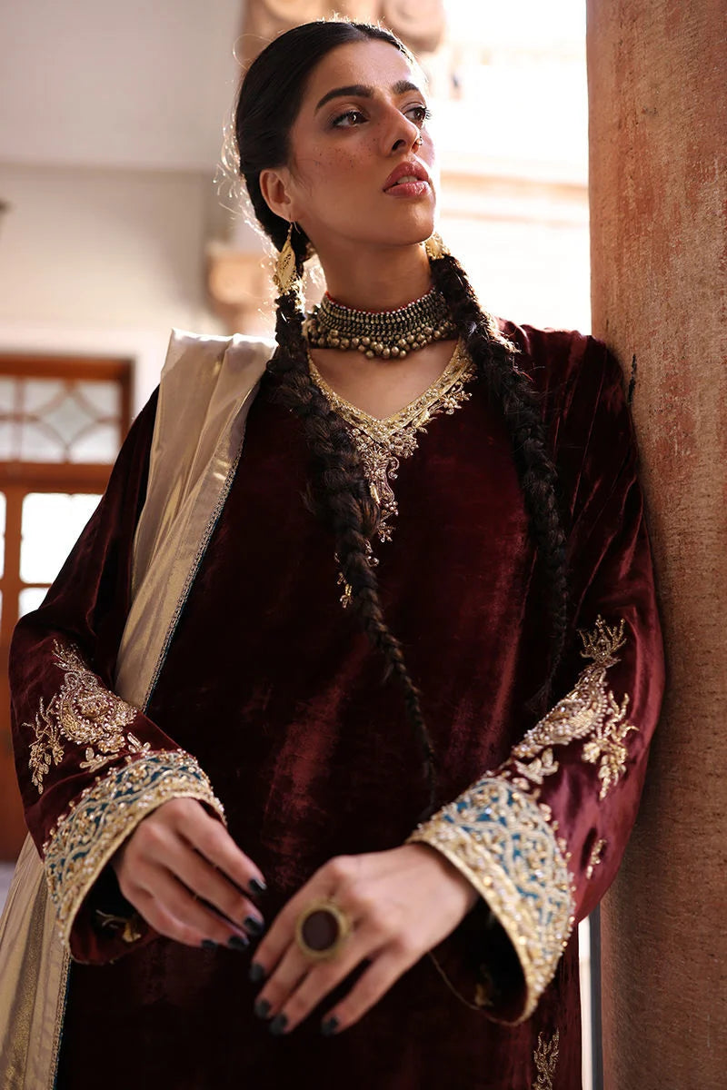 Woman in traditional maroon velvet outfit with gold embroidery indoors