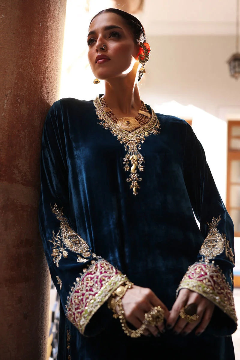 Woman wearing a blue velvet outfit with intricate gold embroidery and jewelry.