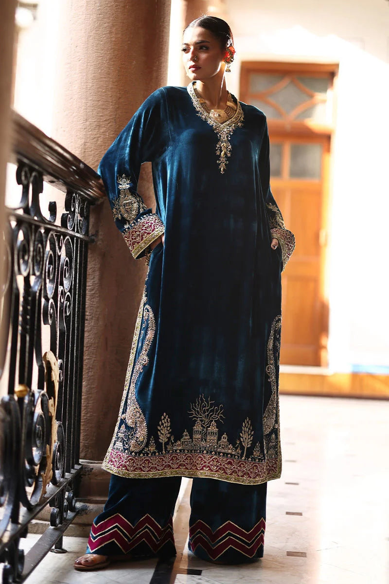 Woman in a traditional blue outfit with intricate patterns standing indoors.