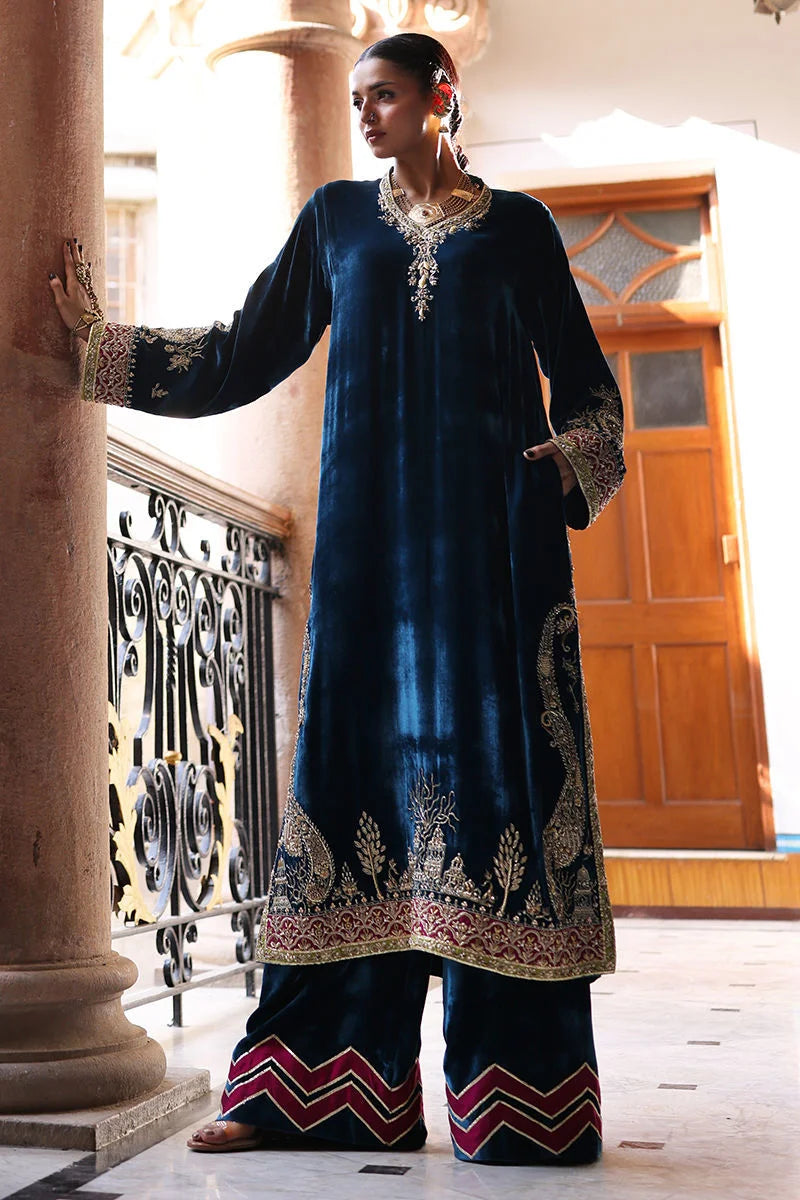 Woman wearing a dark blue embroidered traditional outfit in an elegant interior setting.