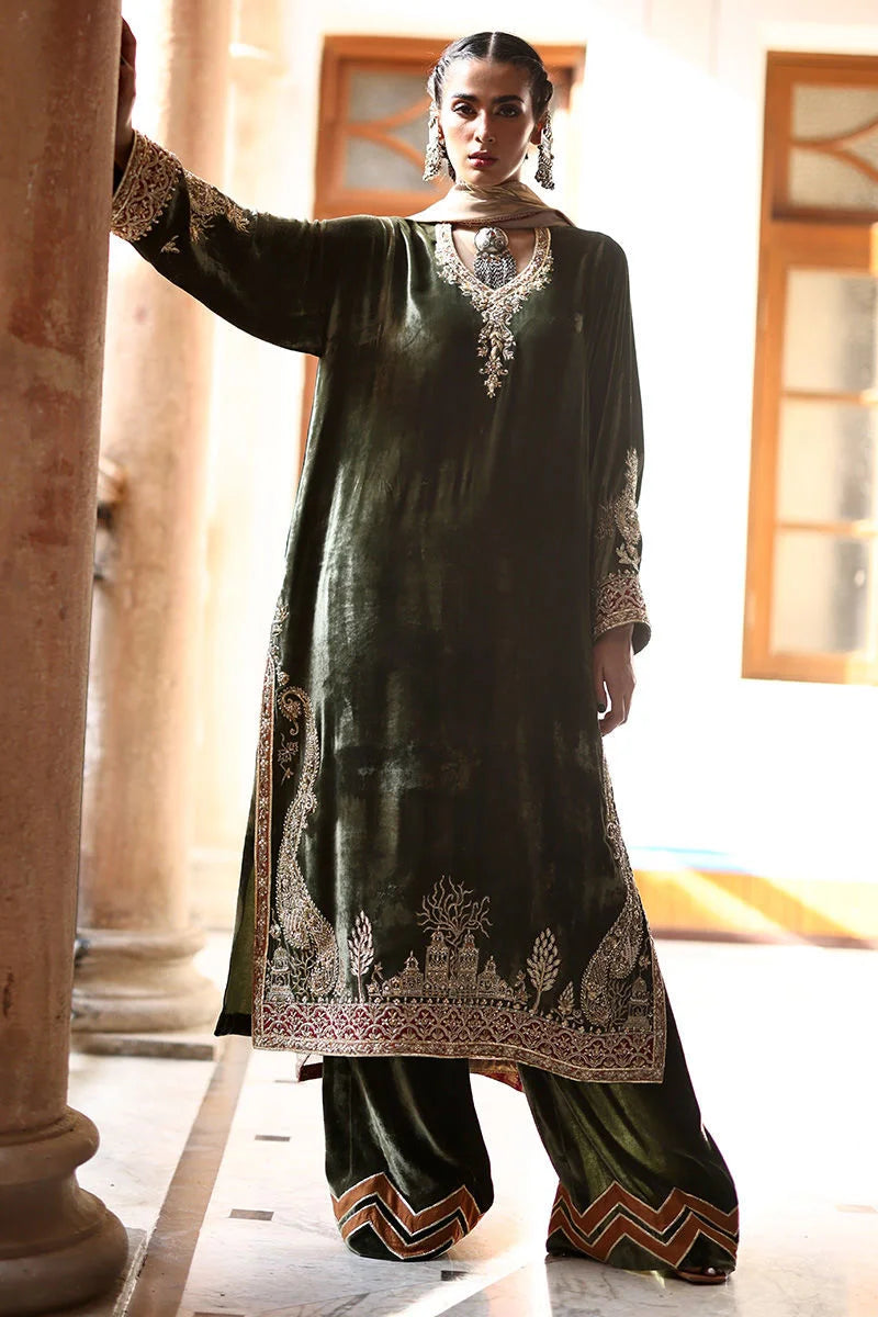 Woman wearing a dark green traditional outfit with intricate embroidery indoors.