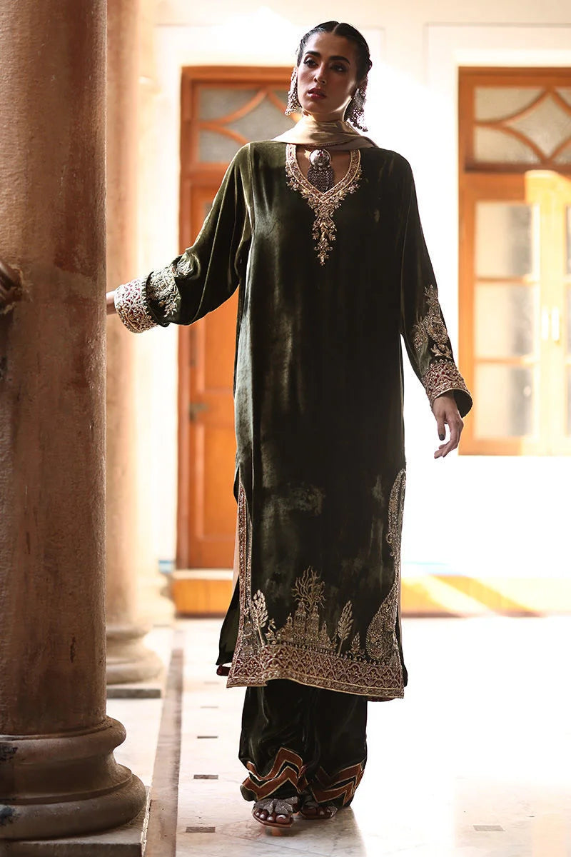 Woman in traditional black and gold outfit with intricate patterns in an indoor setting.