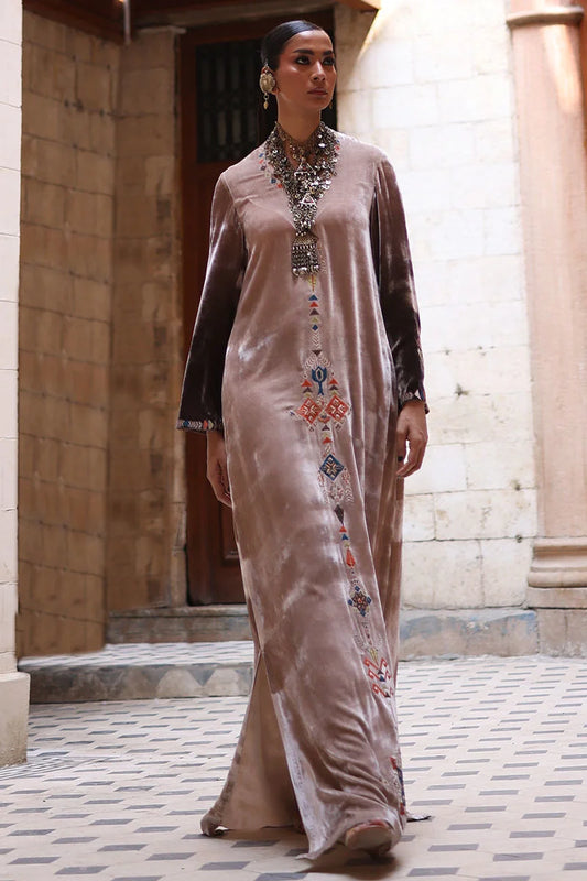 Woman wearing a long, embroidered dress in an outdoor setting with stone walls.