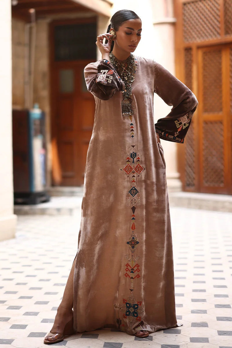 Woman wearing a long, embroidered dress in an indoor setting with wooden columns.