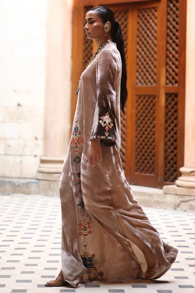 Woman in a long, patterned dress standing in an outdoor setting with architectural elements.