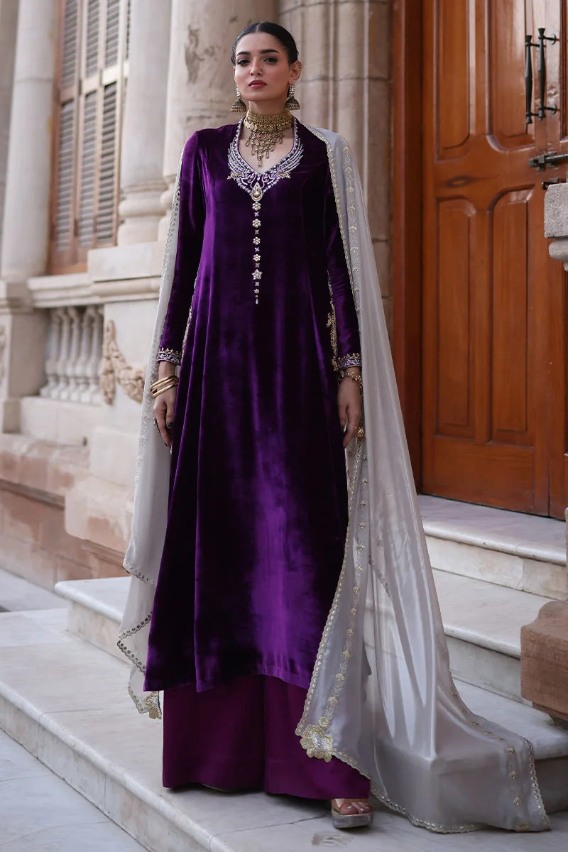 Woman in a purple traditional outfit with a white dupatta standing on steps.