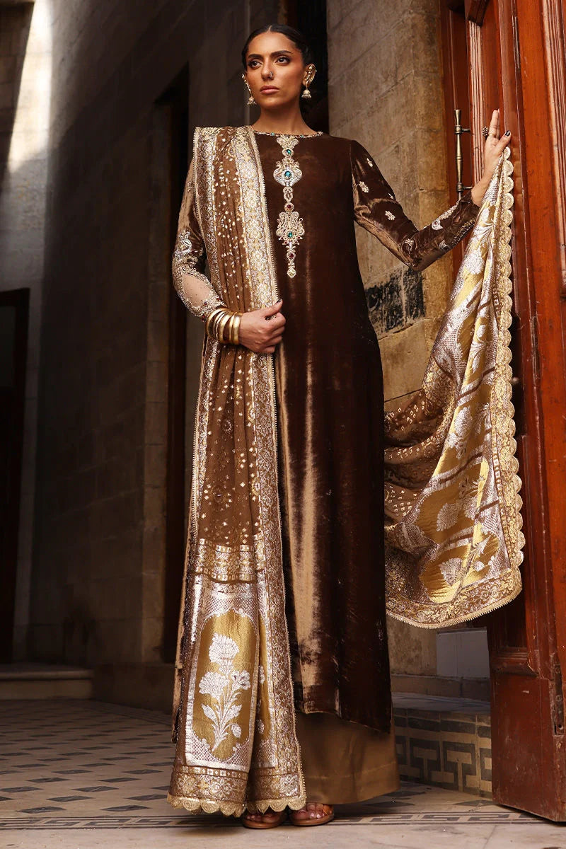 Woman in traditional brown and gold outfit with jewelry, standing indoors.