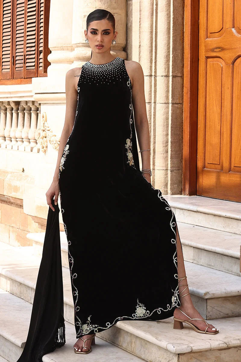 Woman in a black evening gown with floral embroidery standing on steps outside a building.