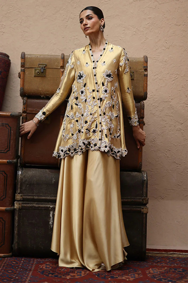 Woman in a gold embroidered outfit standing in front of vintage suitcases.