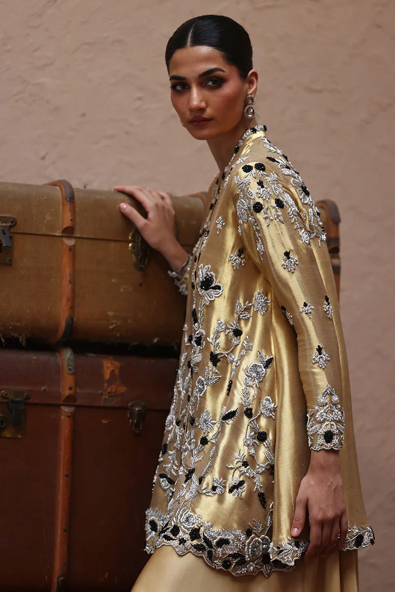 Woman in a gold embroidered outfit standing next to vintage suitcases against a beige wall.