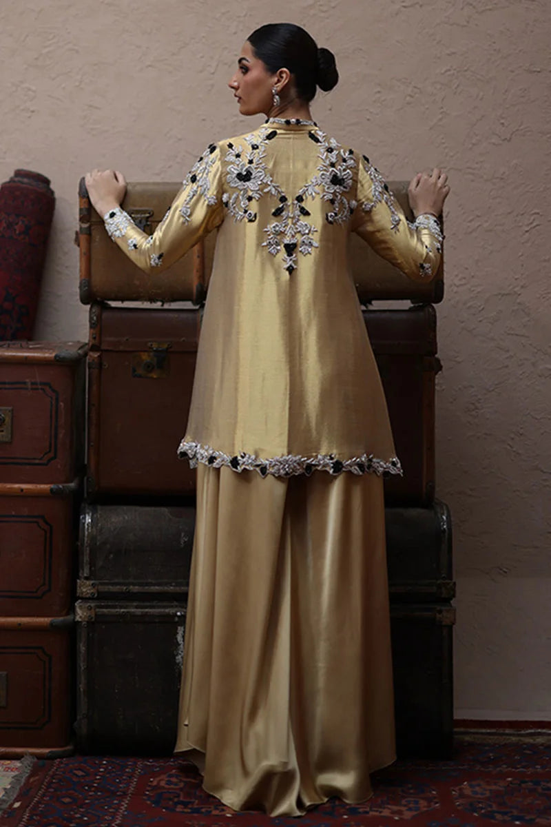 Woman in a beige traditional outfit with intricate patterns standing in front of vintage suitcases.