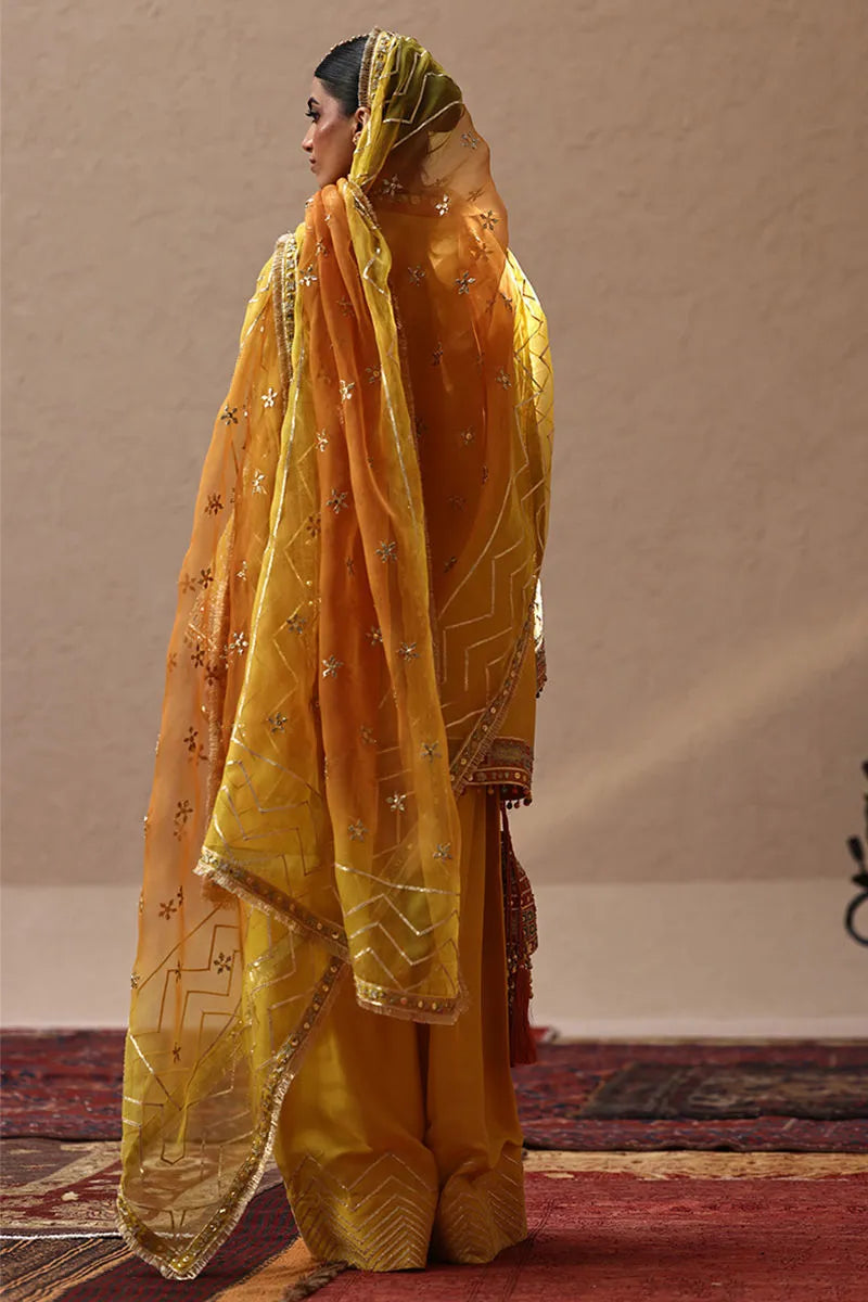 Woman wearing a yellow embroidered traditional outfit with a matching dupatta on a plain background