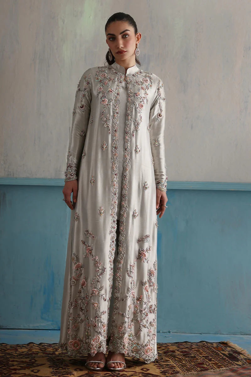Woman wearing a long floral dress against a textured wall with blue baseboard.