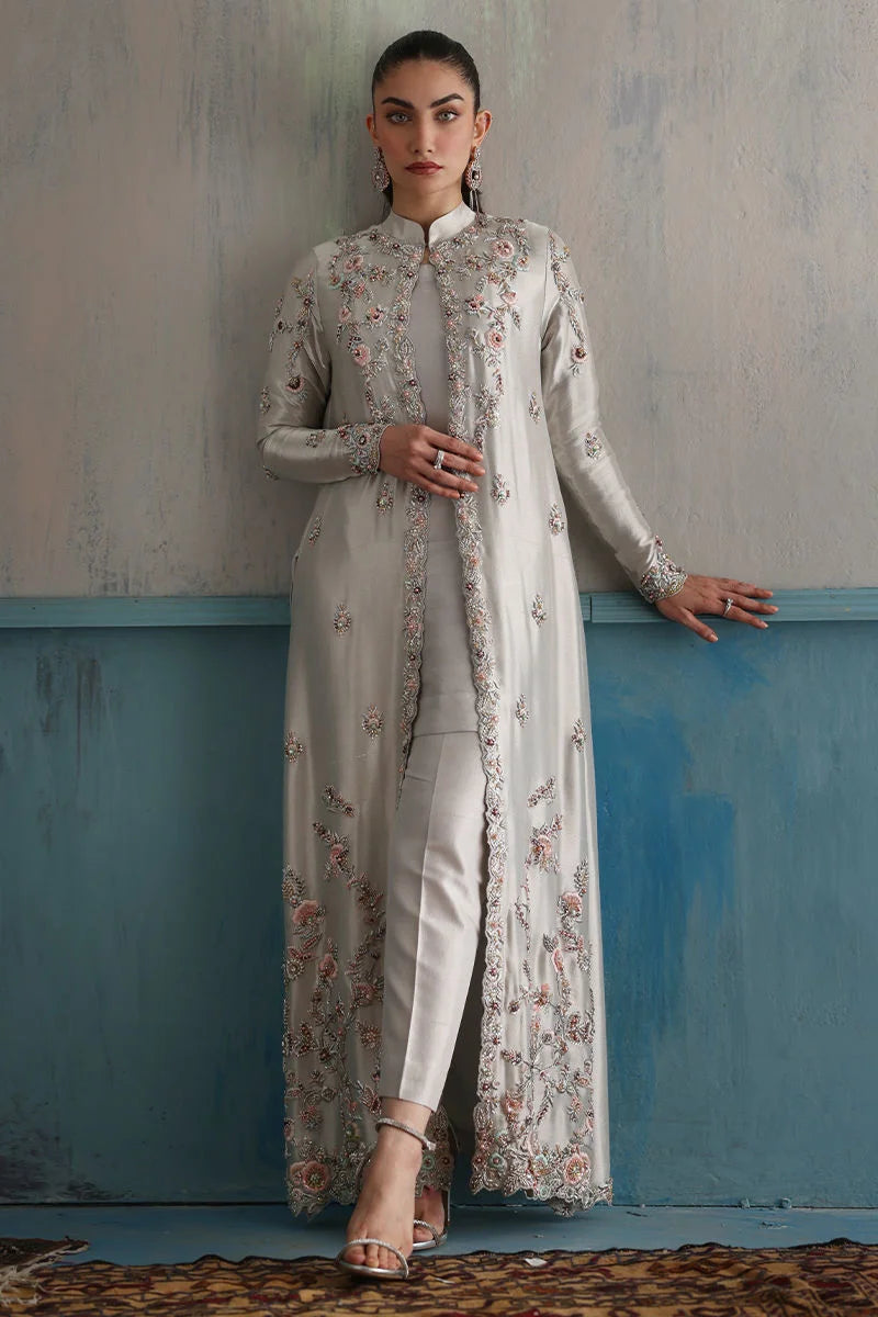 Woman in a traditional outfit with floral patterns against a textured wall.