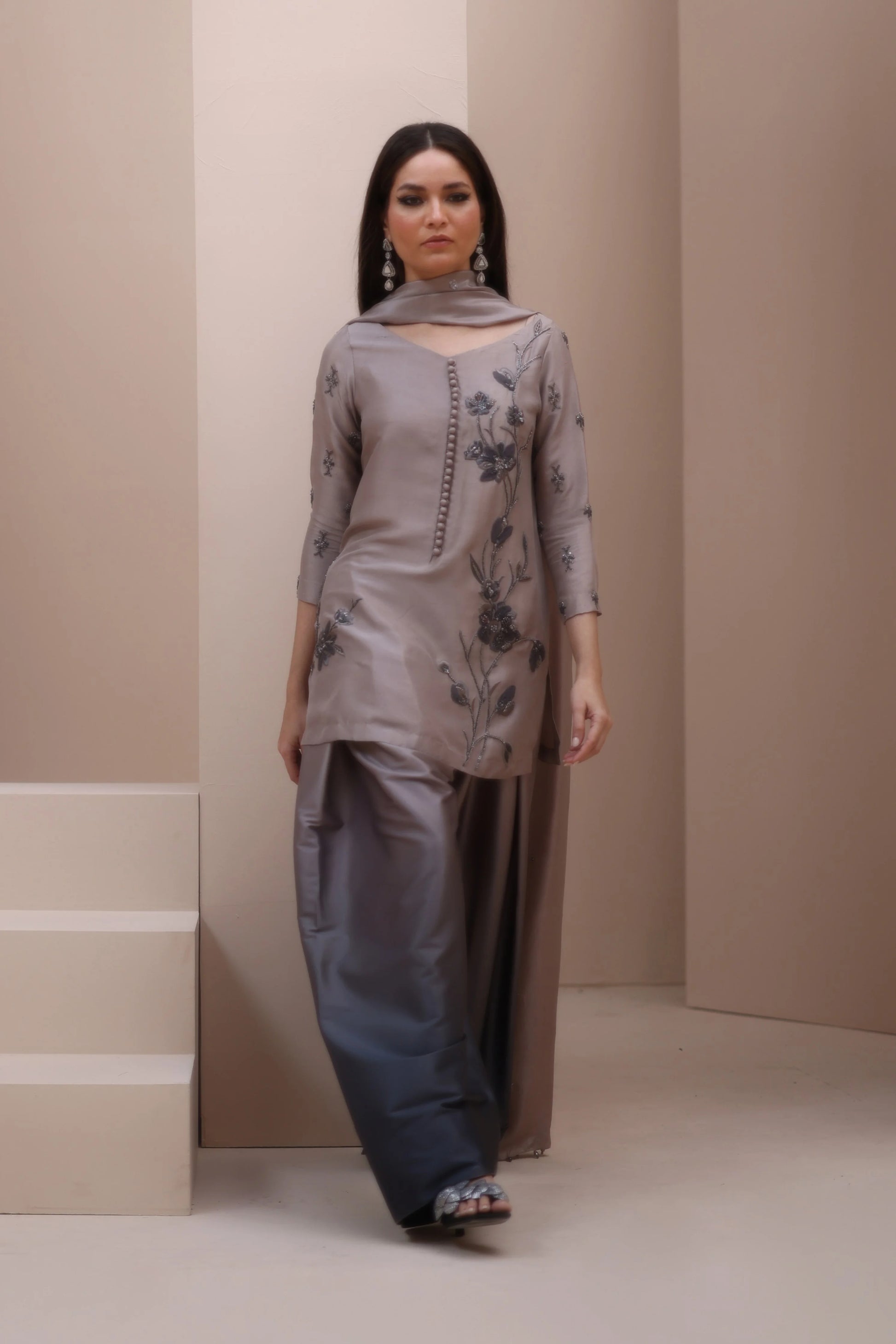 Woman wearing a gray traditional outfit with floral patterns against a beige background