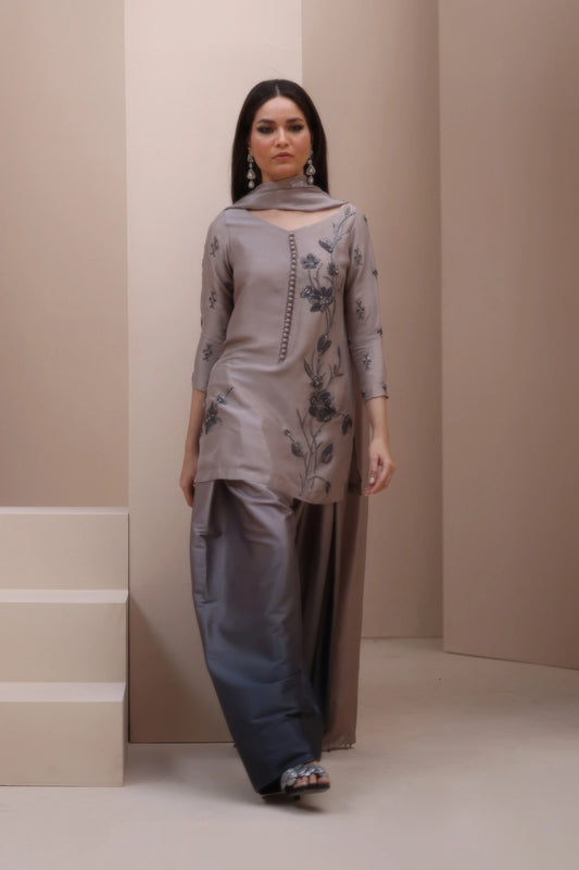 Woman wearing a gray traditional outfit with floral patterns against a beige background