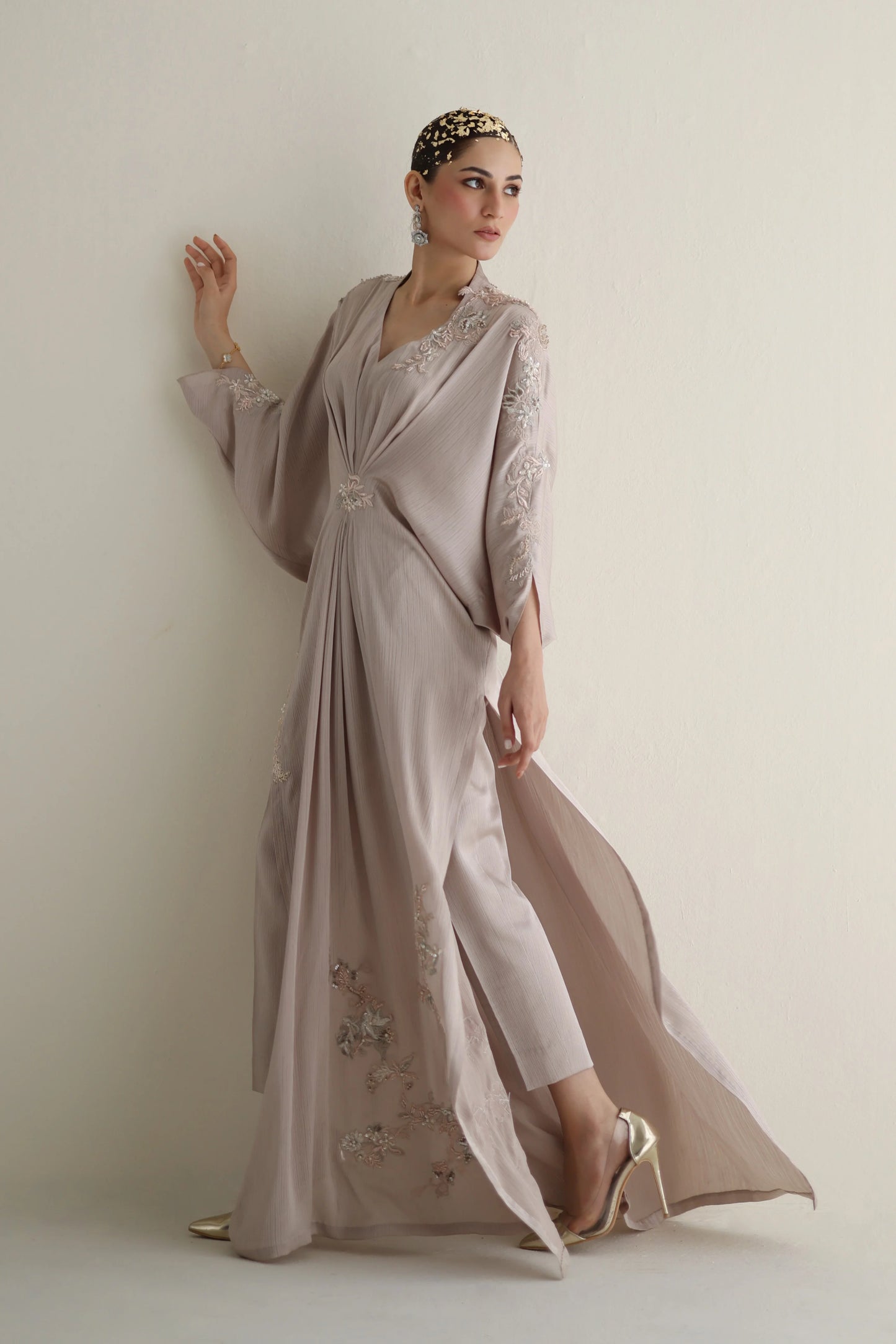 Woman wearing a long, elegant dress with floral embellishments against a plain background