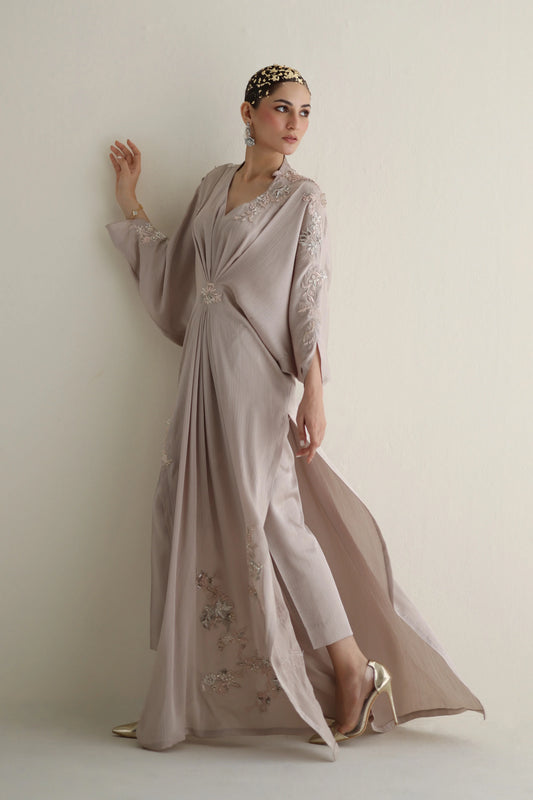 Woman wearing a long, elegant dress with floral embellishments against a plain background