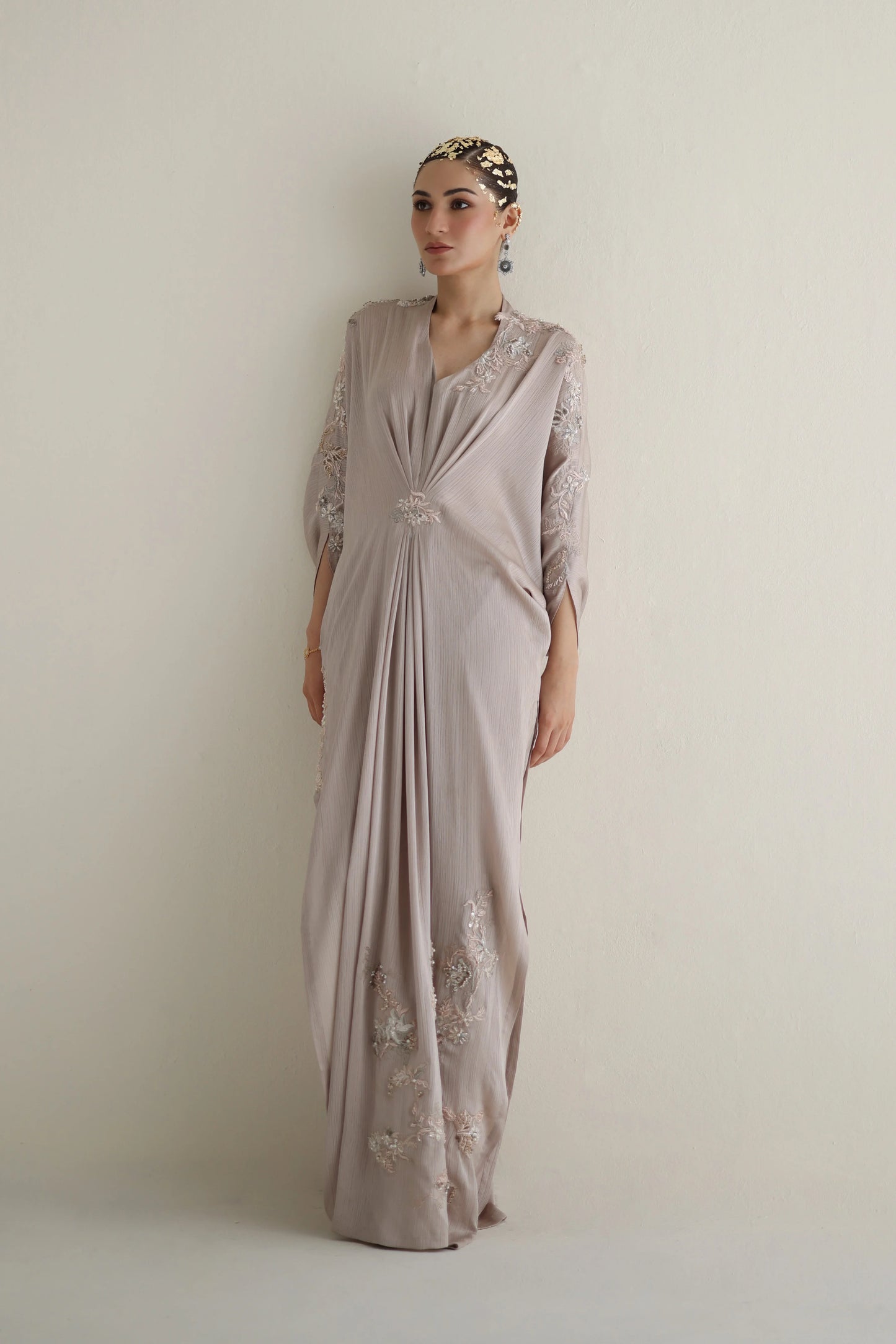 Woman wearing a long, light-colored dress with lace details against a plain background