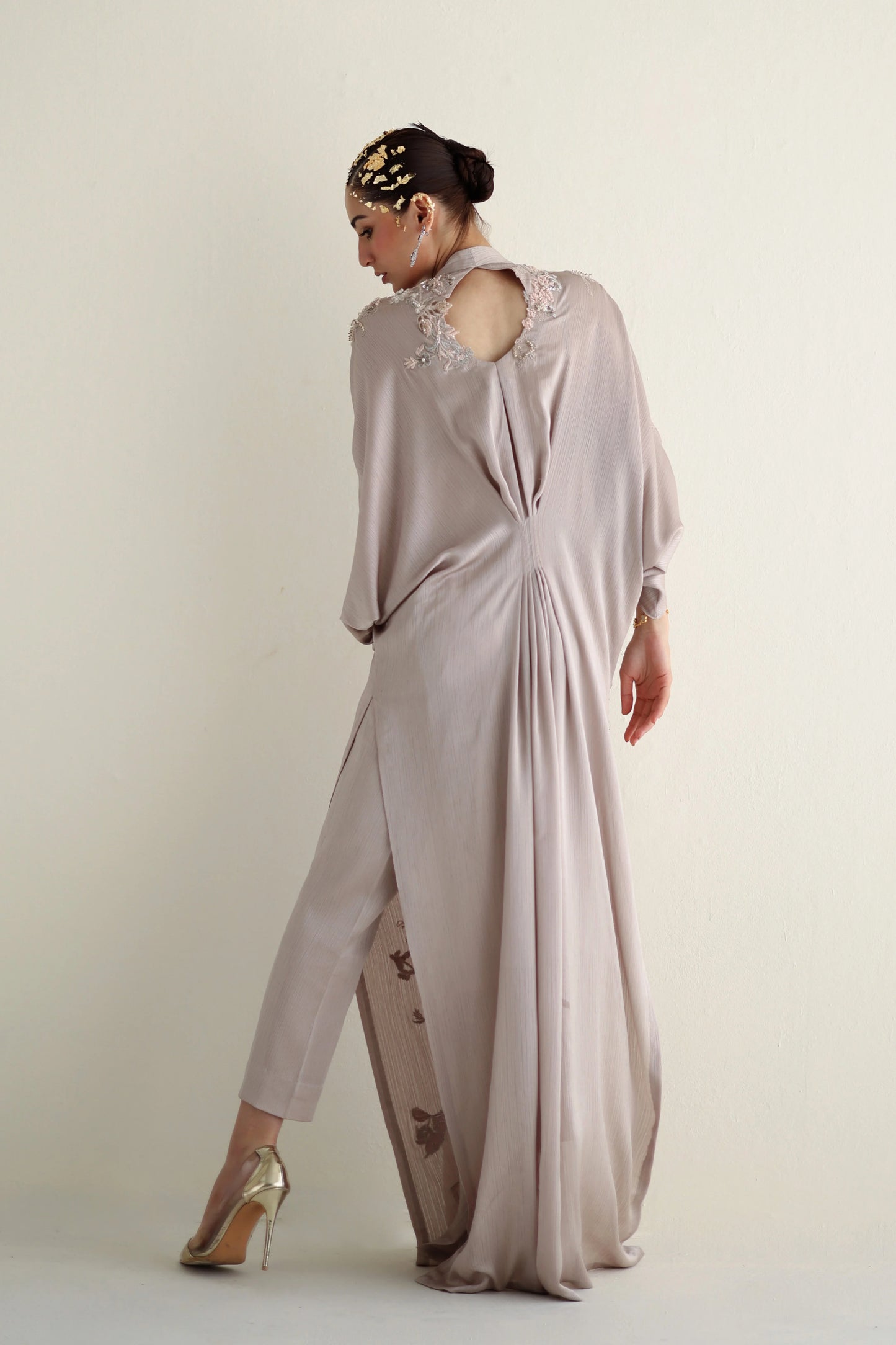 Woman wearing a long, light-colored dress with a sheer overlay against a plain background