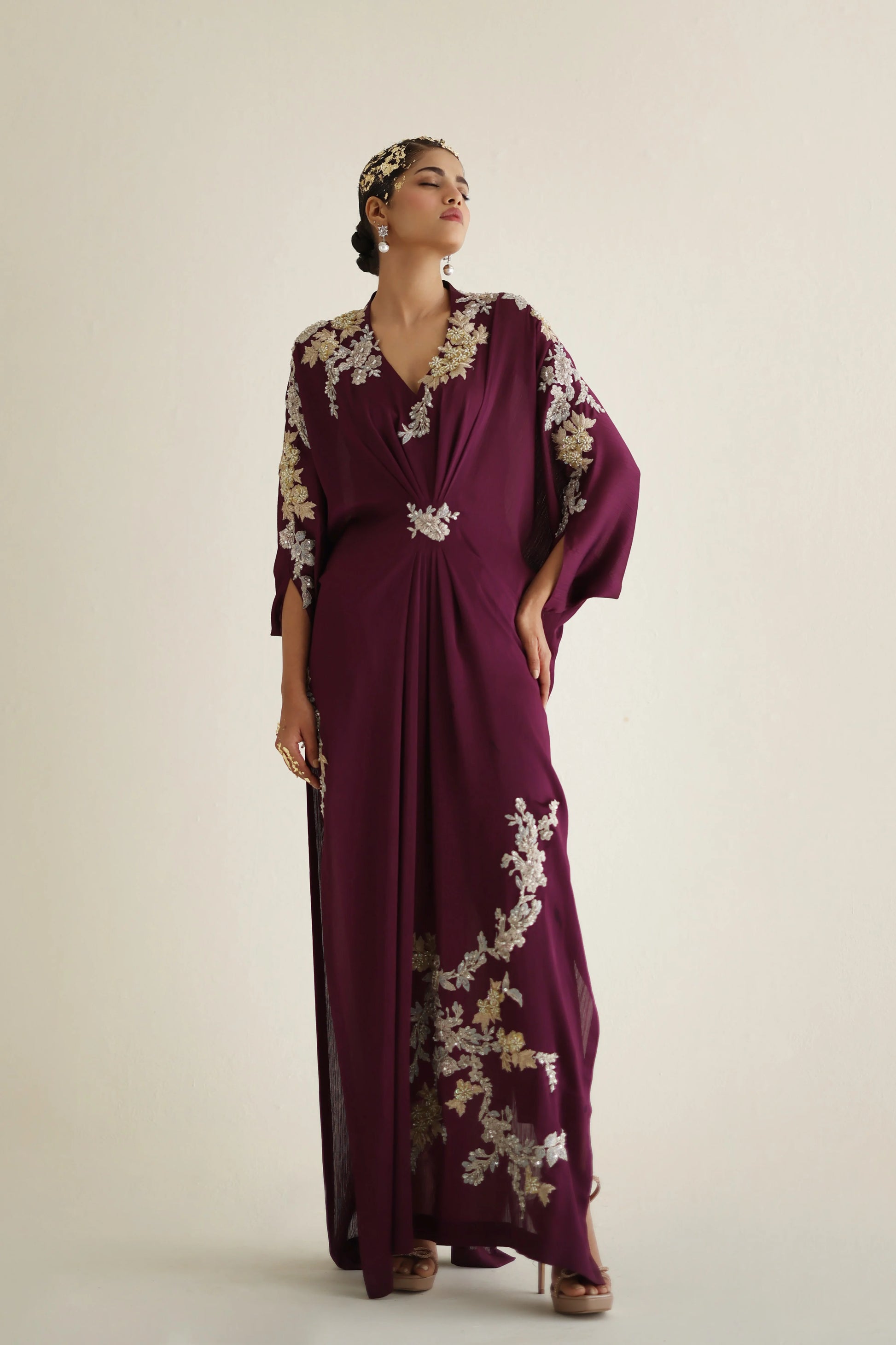 Woman wearing a burgundy dress with floral embroidery on a beige background