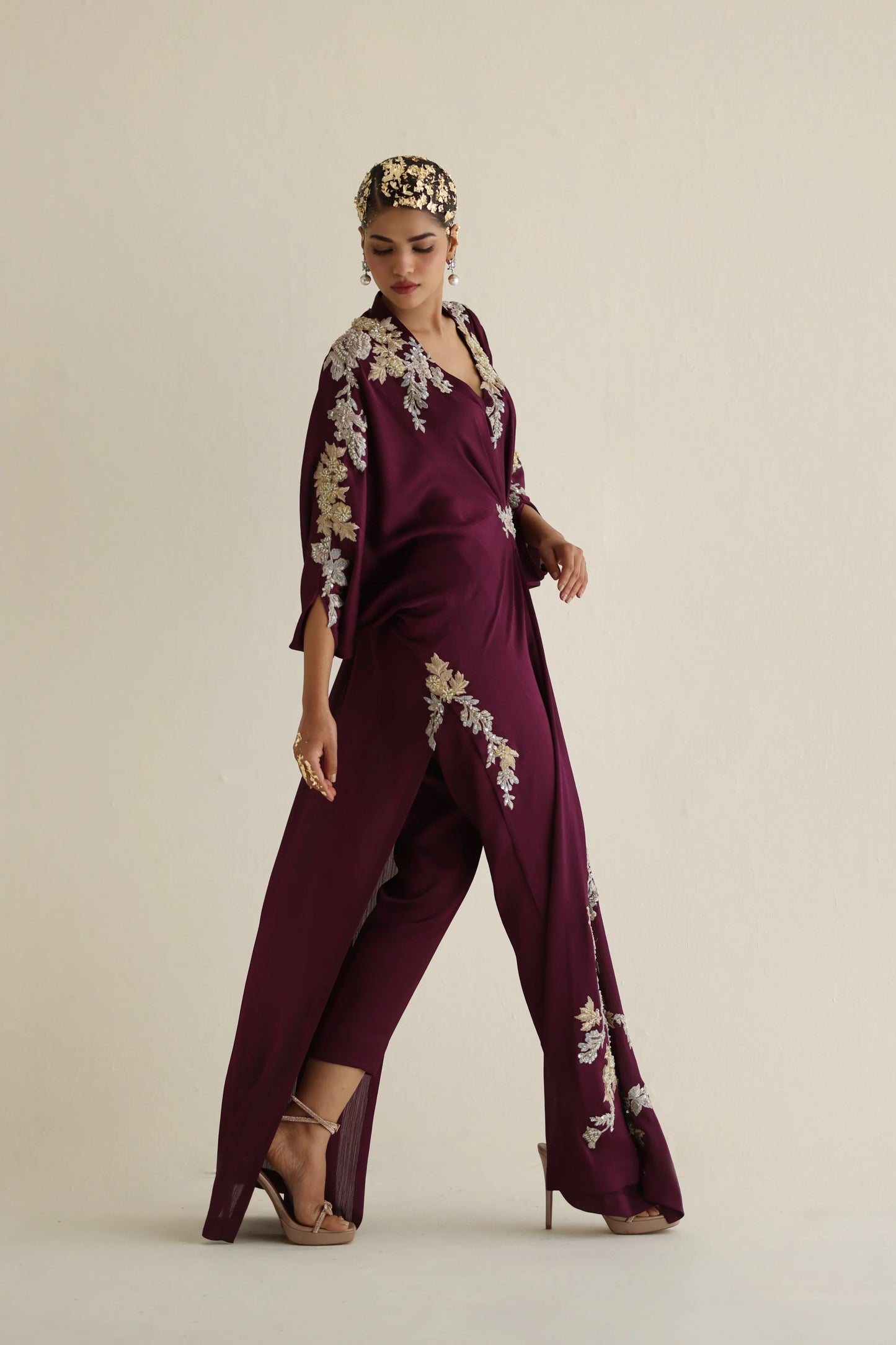 Woman wearing a burgundy jumpsuit with floral embroidery on a beige background