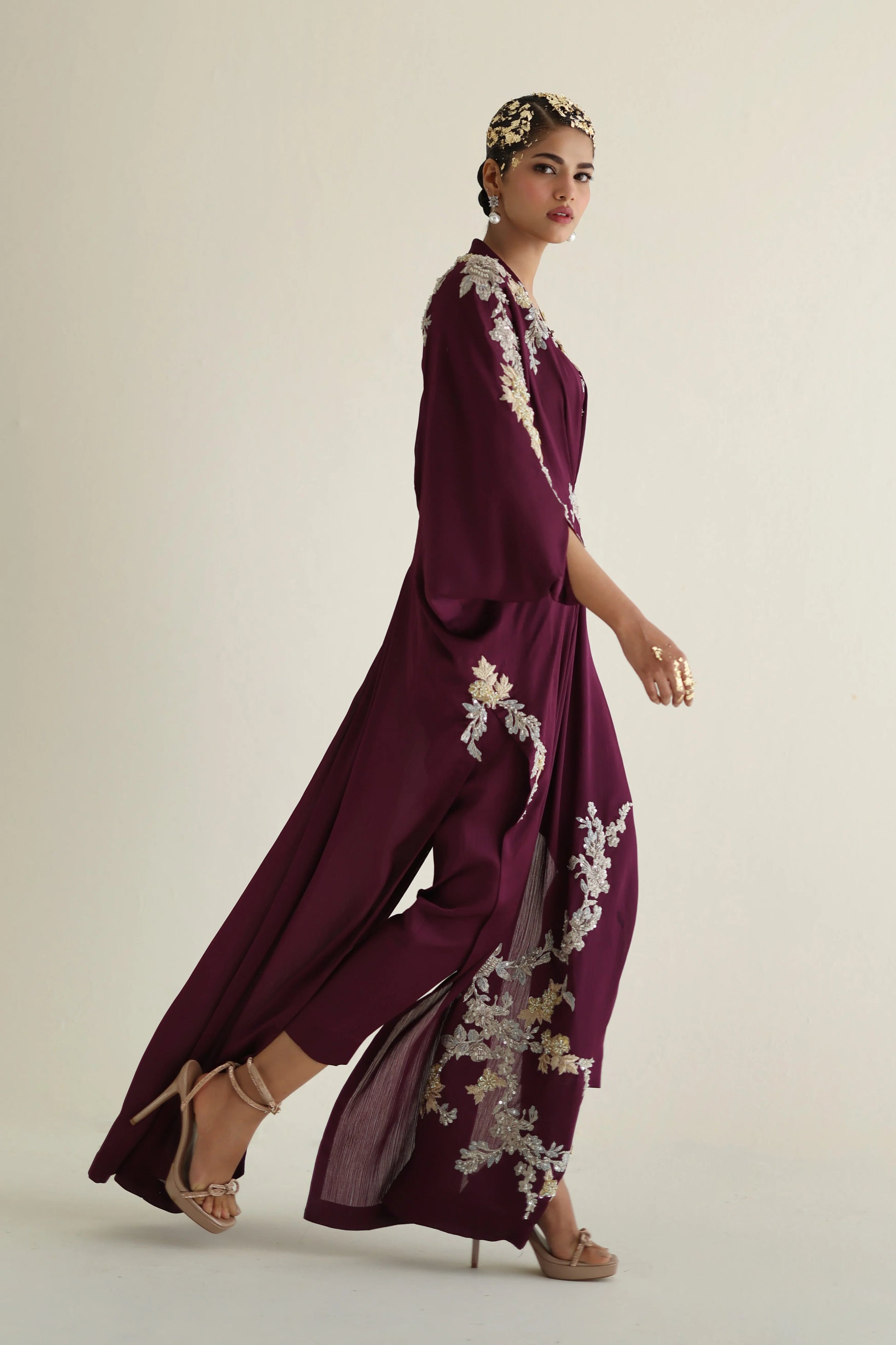 Woman wearing a burgundy outfit with floral embroidery on a plain background