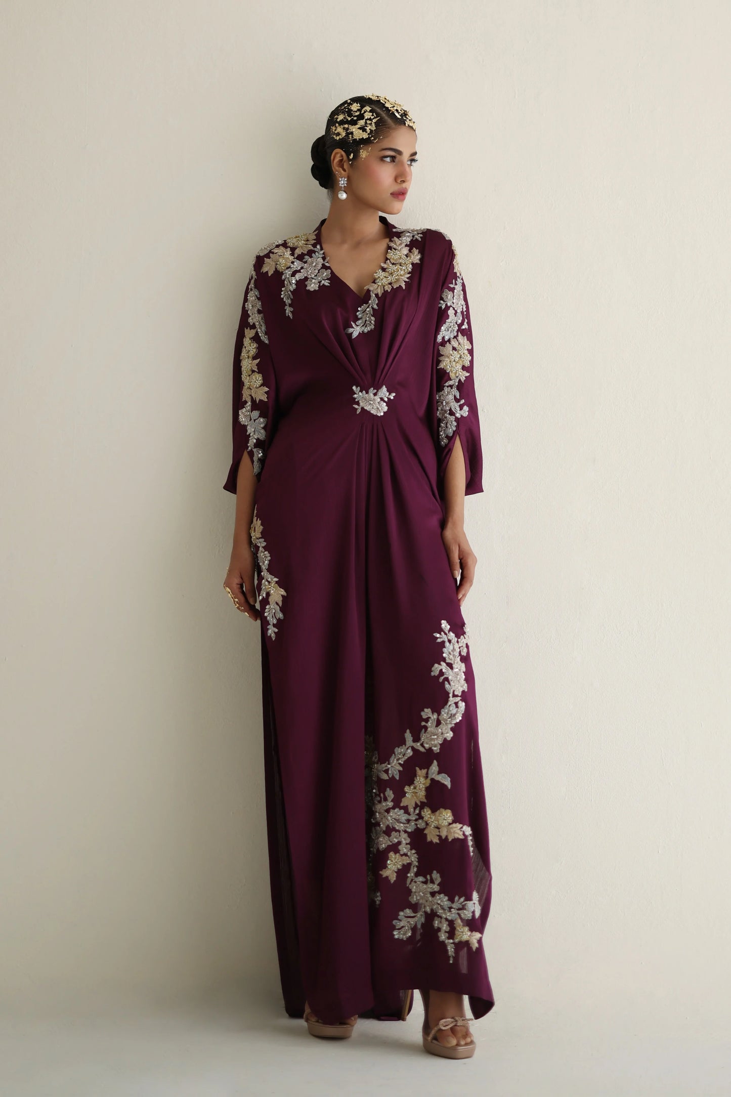 Woman wearing a long, dark purple dress with floral patterns on a plain background