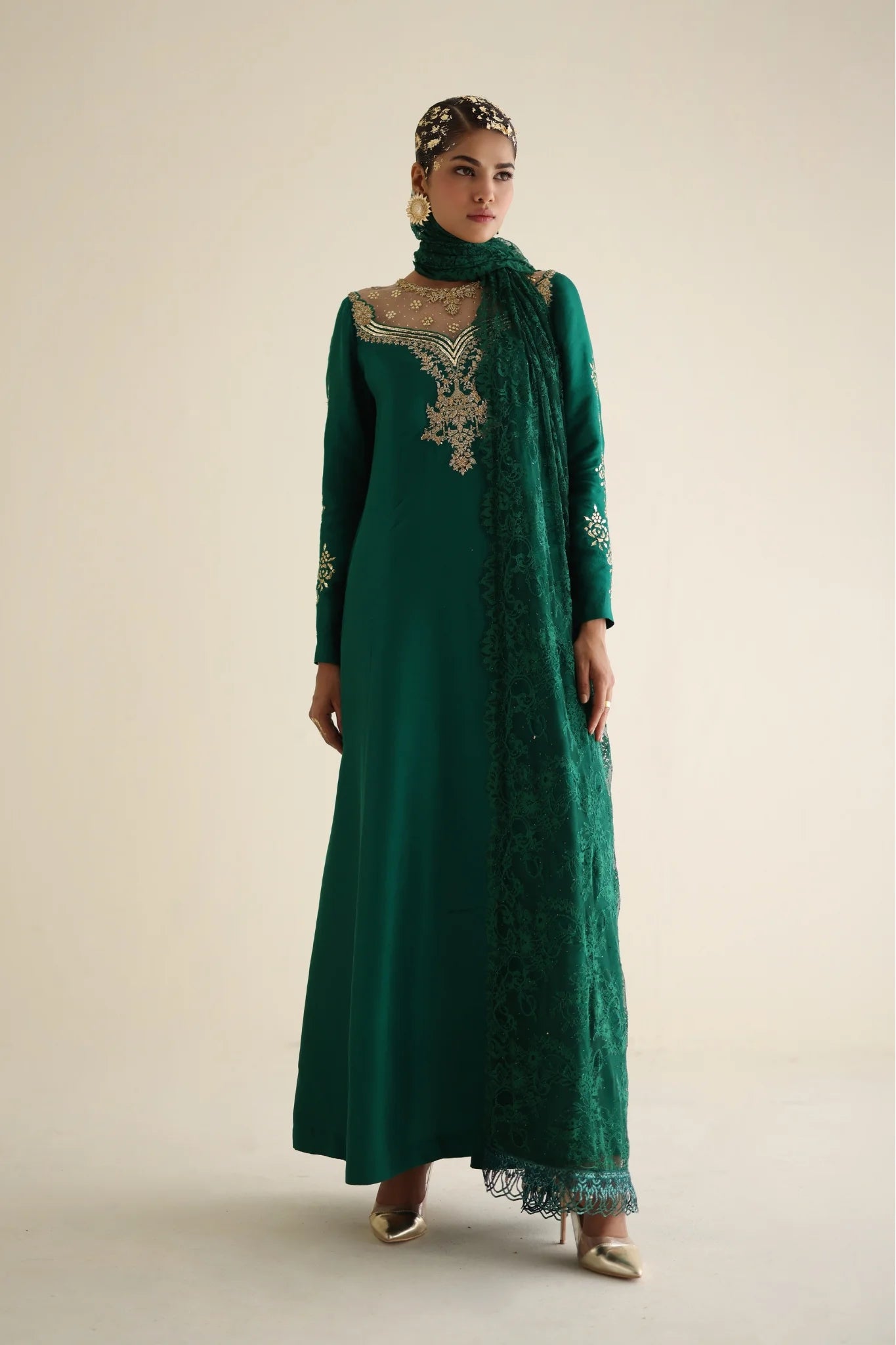 Woman wearing a green embroidered dress with a matching headscarf on a beige background