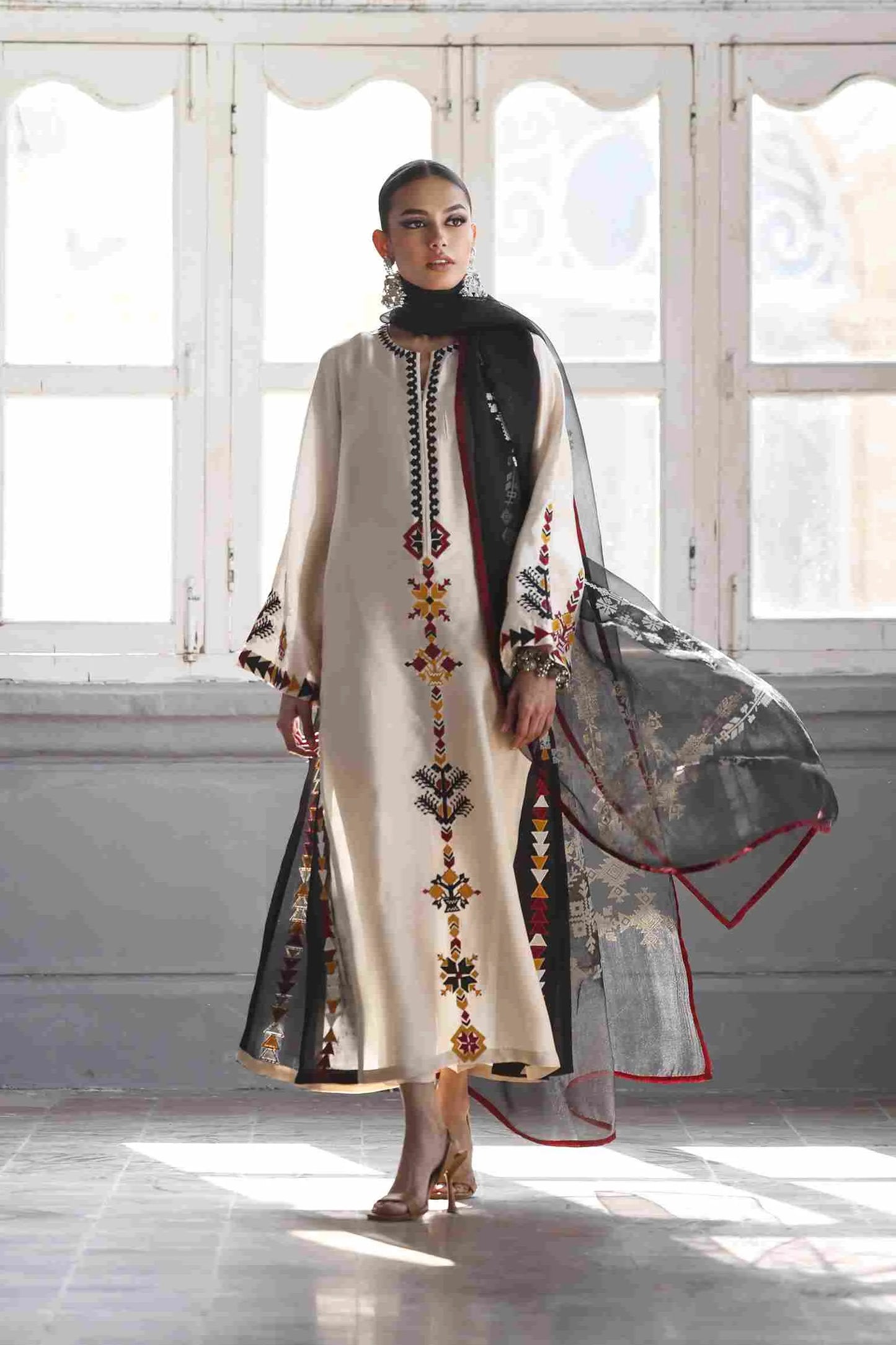Woman holding a traditional outfit with intricate designs in a bright room.