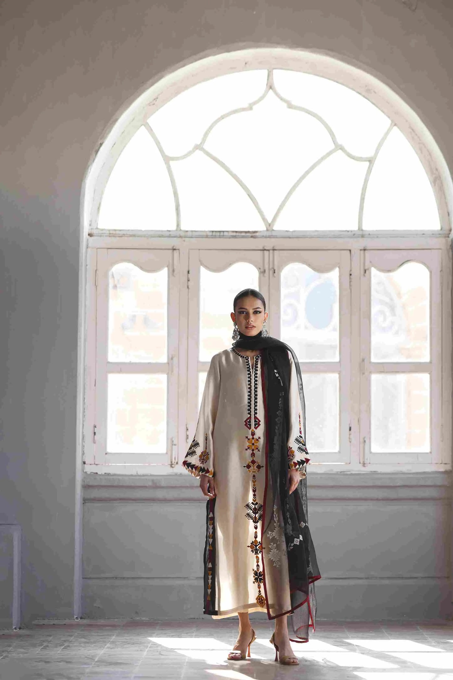 Woman in a long, ornate dress standing in a room with large windows.