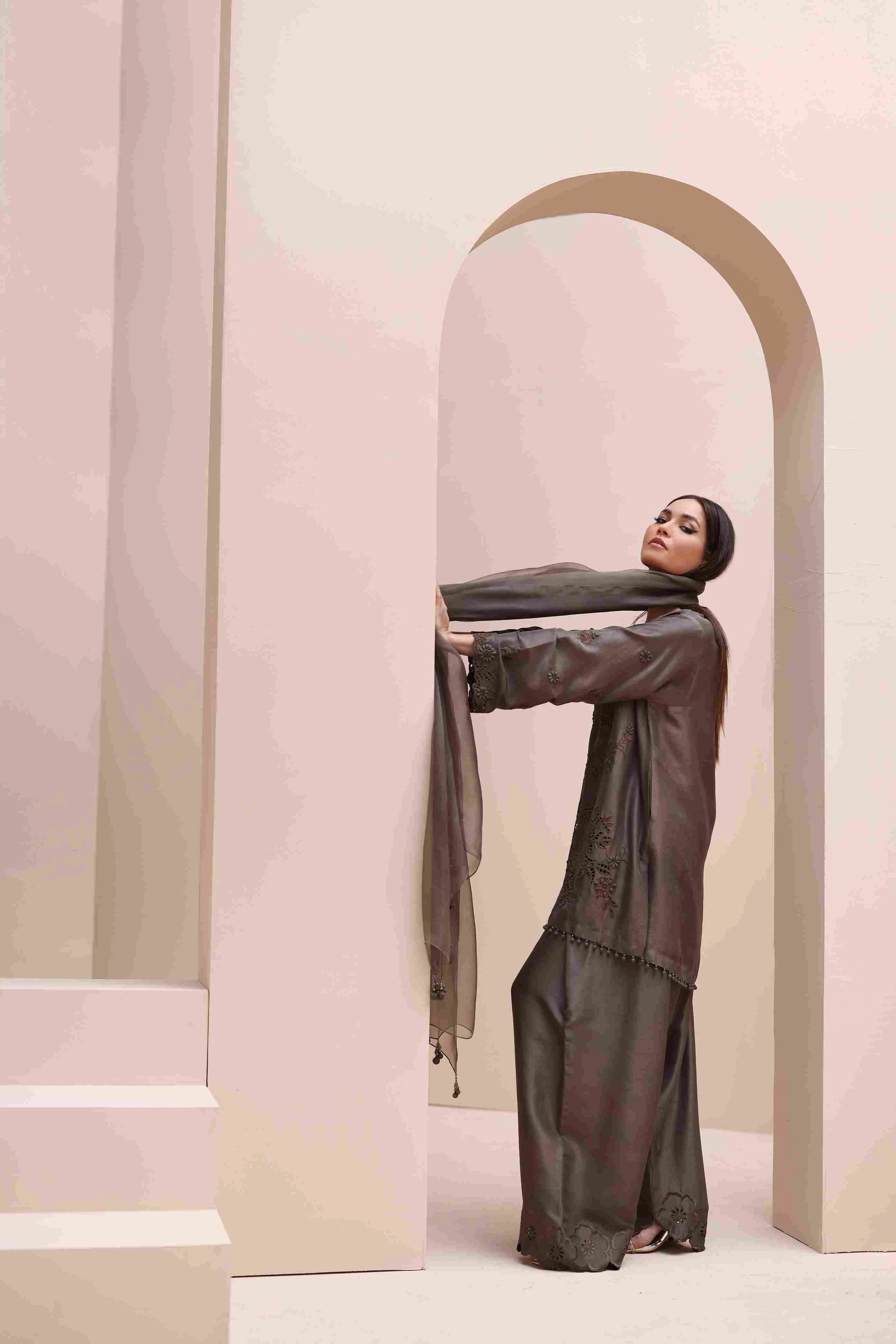 Woman in a long, dark green dress standing against a light pink archway.