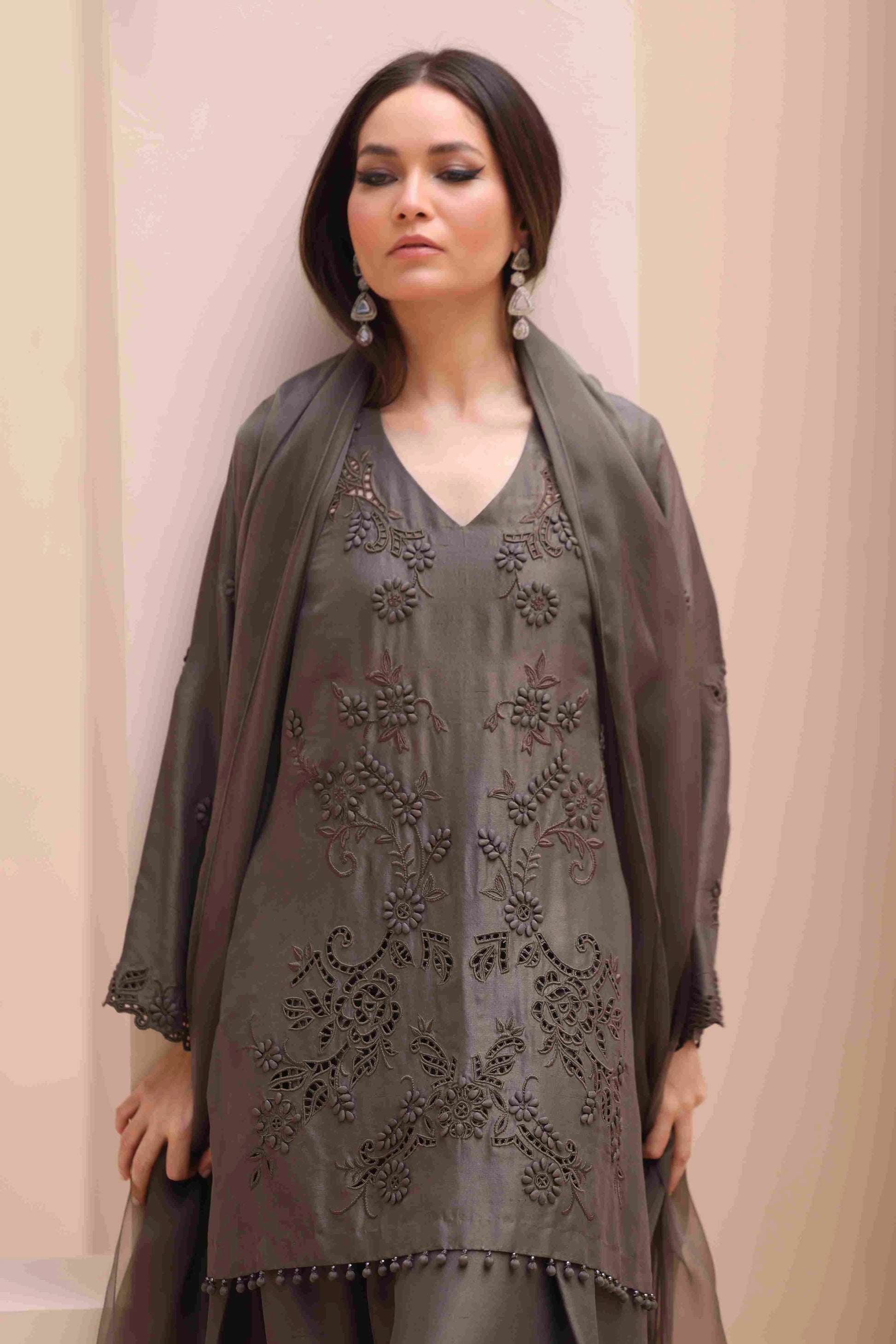 Woman wearing a gray embroidered outfit with a matching shawl against a beige background
