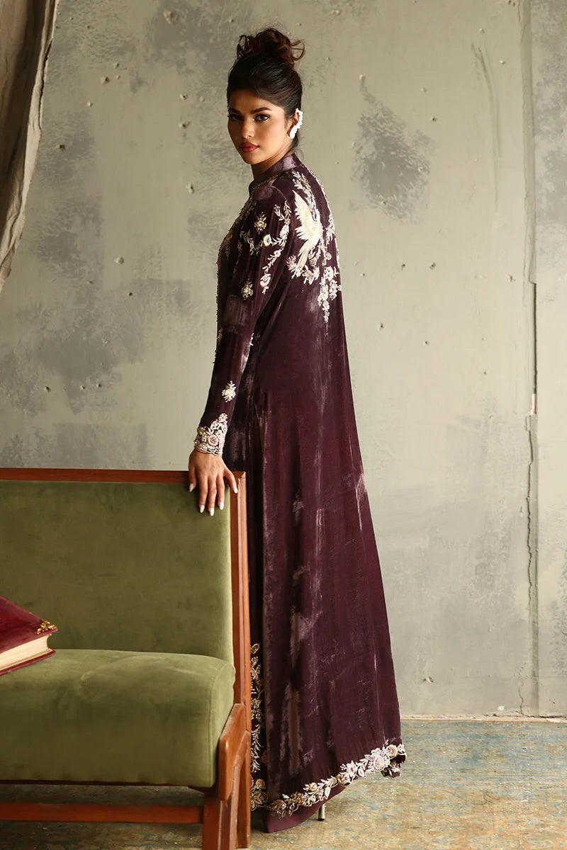 Woman in a long, dark-colored dress with floral patterns standing against a textured wall.