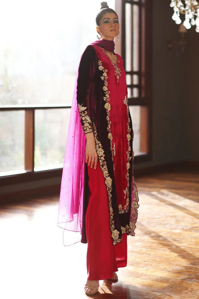 Woman wearing a red and black traditional outfit with a pink dupatta in a room with large windows.