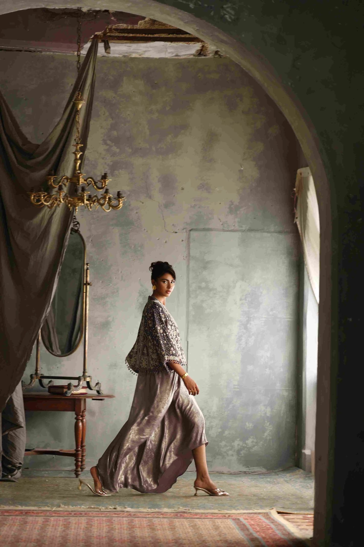 Woman in a patterned dress walking through an archway in a room with peeling paint.