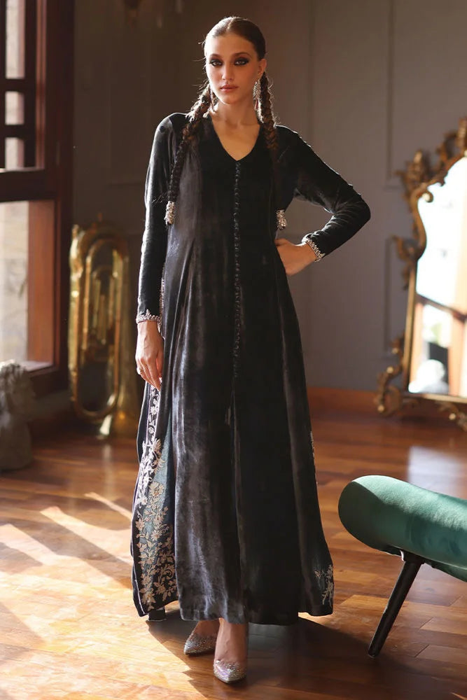 Woman in a long black dress standing in a room with wooden floor and decorative elements.