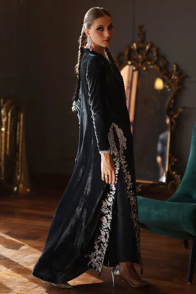 Woman in a long black dress with white lace details standing in a room with a mirror and chair.