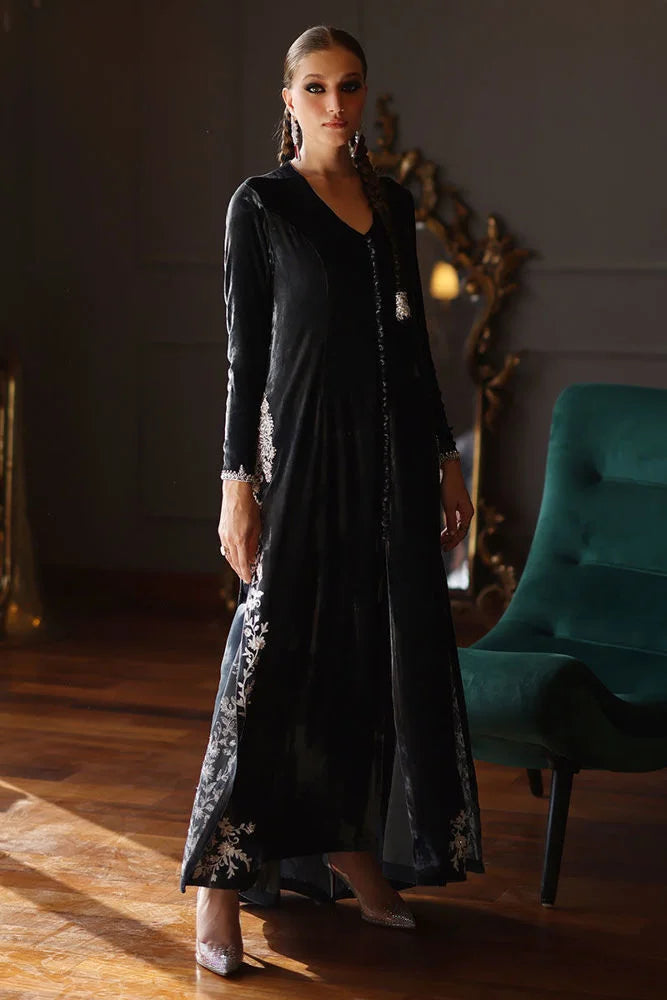 Woman in a black dress with floral patterns standing in a room with a teal chair and decorative items.