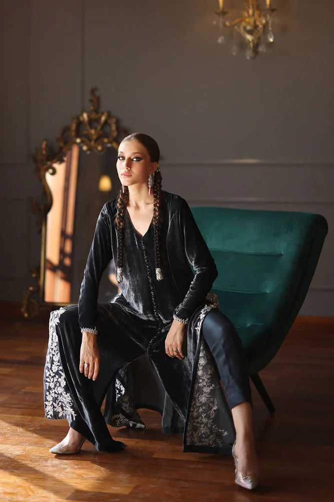 Woman in a black outfit sitting on a green chair in an elegant room.