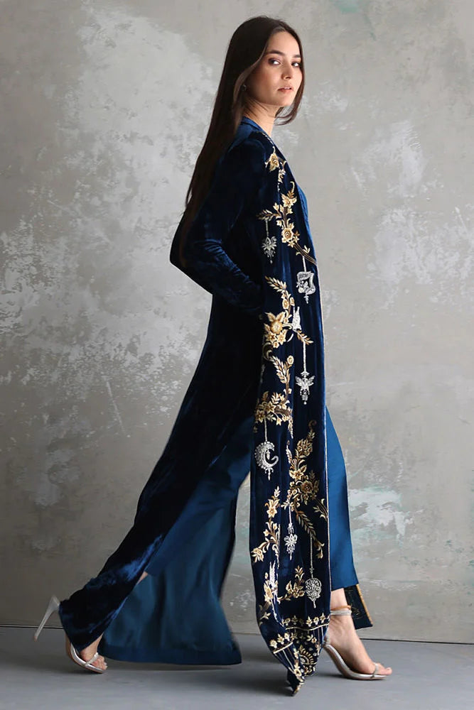 Woman wearing a long, dark blue embroidered dress against a gray background
