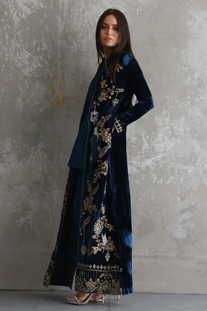 Woman wearing a long, dark blue embroidered coat against a gray background