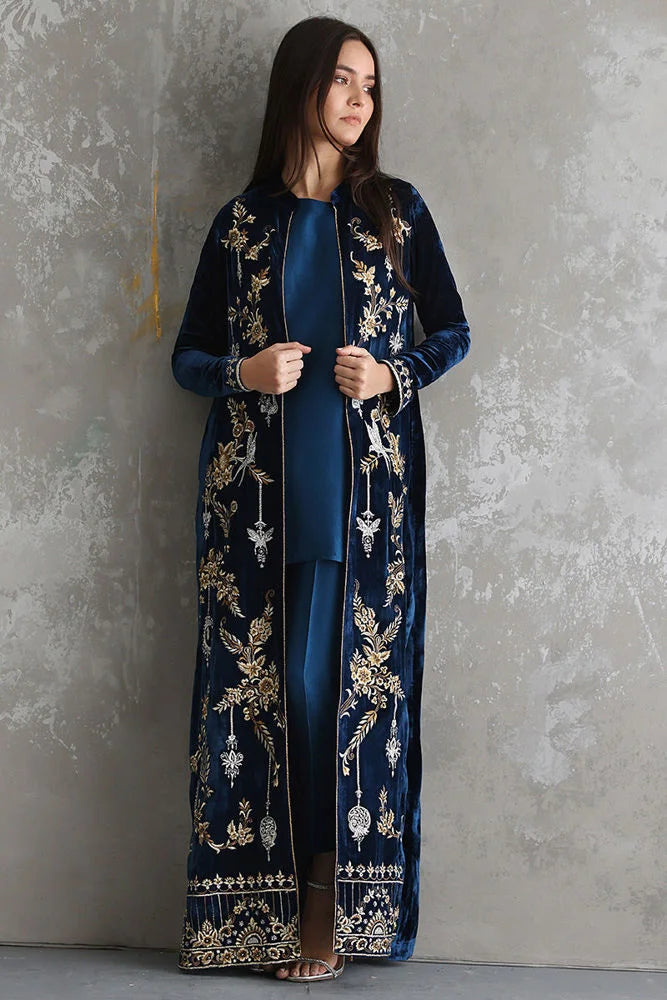 Woman wearing a dark blue embroidered outfit against a gray textured wall.