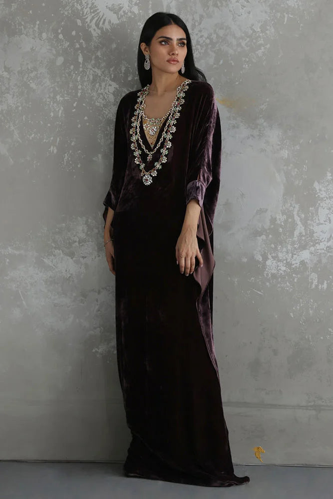 Woman wearing a dark purple dress with intricate detailing against a textured gray wall.
