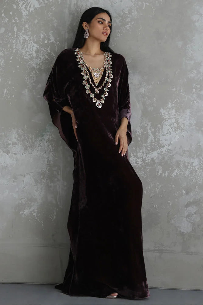 Woman wearing a dark velvet dress with intricate jewelry against a textured gray wall.