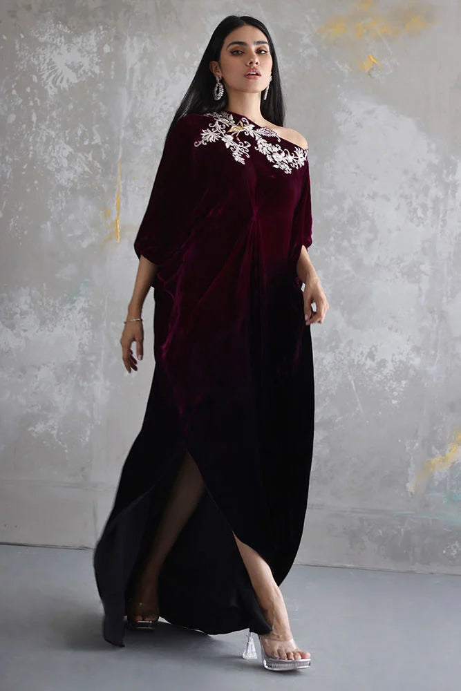 Woman wearing a burgundy velvet dress with floral embroidery against a gray textured wall.