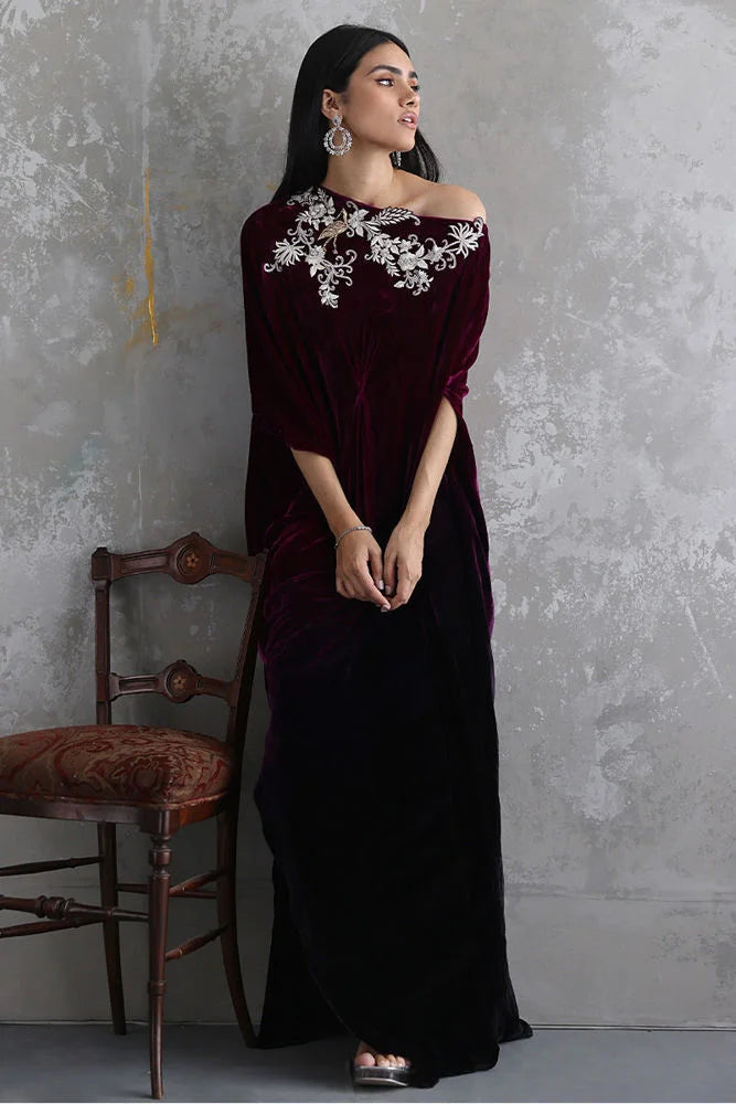 Woman wearing a dark red velvet dress with floral embroidery against a gray wall.