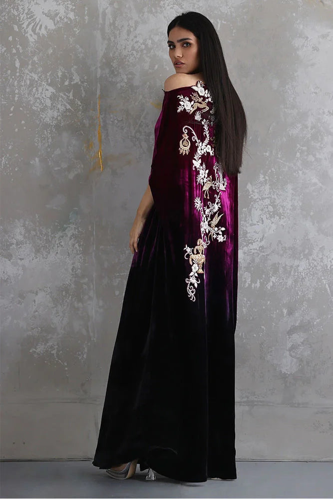 Woman wearing a dark purple dress with white floral embroidery against a textured gray wall.